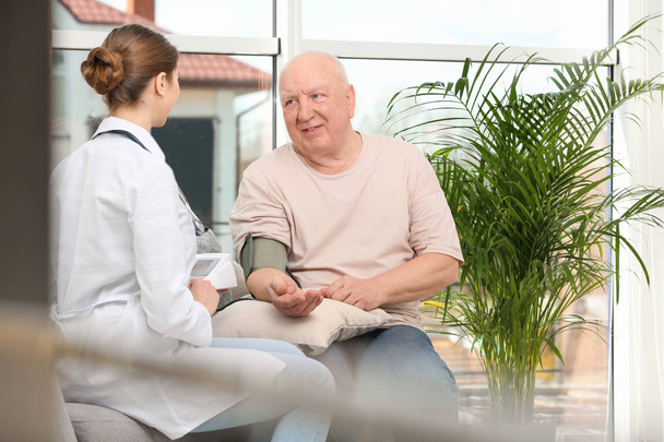 Nurse measuring blood pressure of elderly man in living room. Assisting senior generation - Foto, imagen