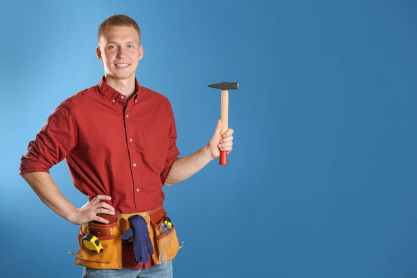Handsome young working man with hammer against color background, space for text - Foto, imagen