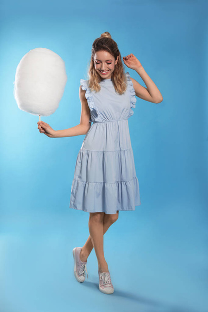 Full length portrait of pretty young woman with tasty cotton candy on blue background - Valokuva, kuva