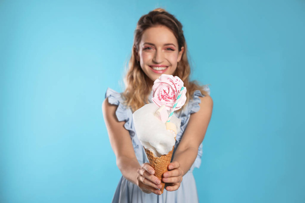 Portrait of young woman holding cotton candy dessert on blue background - Фото, зображення