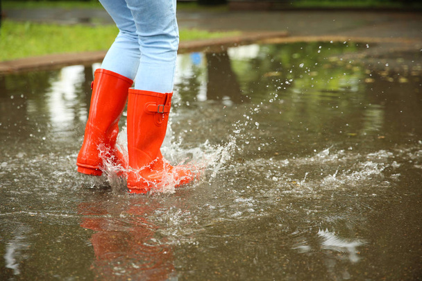 Woman with red rubber boots jumping in puddle, closeup. Rainy weather - Φωτογραφία, εικόνα