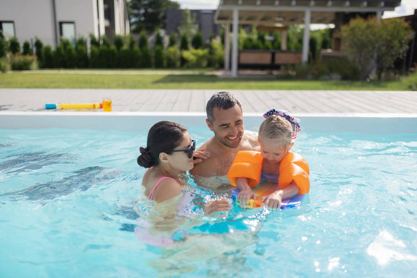 Padres felices sintiéndose increíbles nadando en la piscina con su hija
 - Foto, Imagen