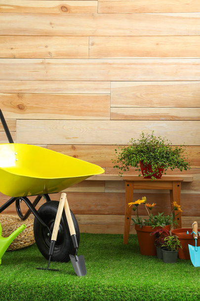 Wheelbarrow with gardening tools and flowers near wooden wall. Space for text - Foto, Imagem