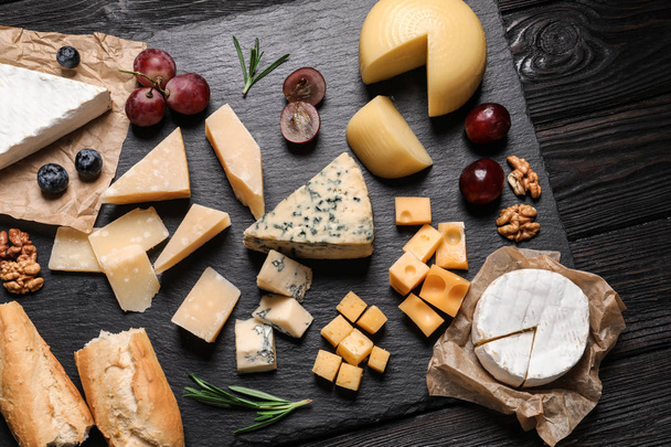 Flat lay composition with different types of delicious cheese on slate board - Foto, Imagen