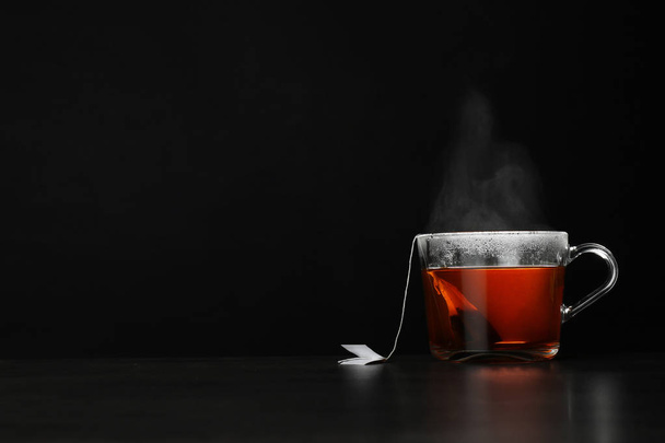 Glass cup of hot tea on table against black background, space for text - Photo, Image