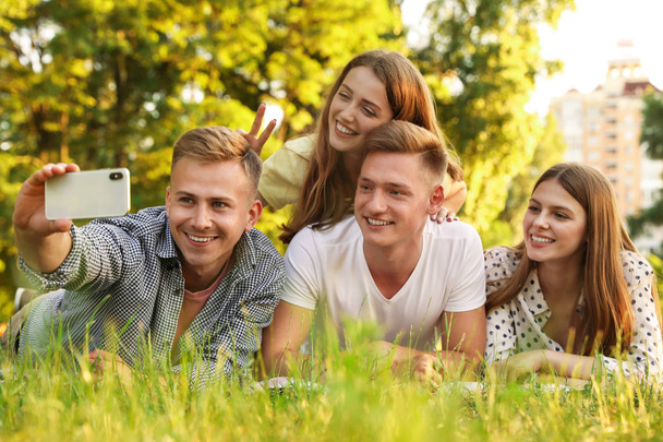 Giovani che fanno selfie mentre fanno un picnic nel parco durante la giornata estiva
 - Foto, immagini