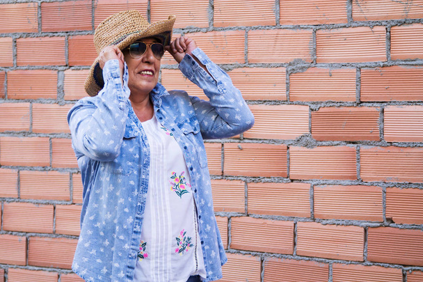 retrato de mujer mayor con sombrero y gafas de sol con pared de ladrillo
 - Foto, imagen