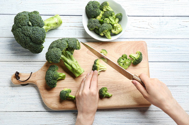 Woman cutting fresh green broccoli with knife on white wooden table, top view - Foto, immagini