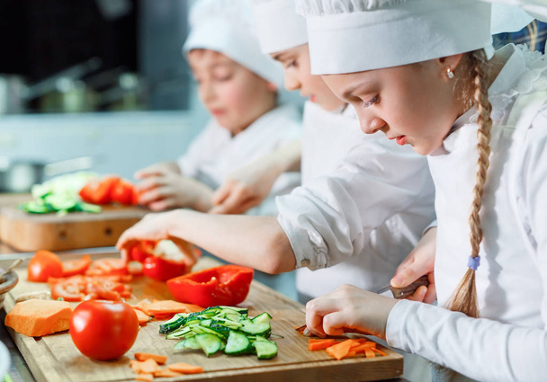 Children in chefs hat grind vegetables on the kitchen. - Valokuva, kuva