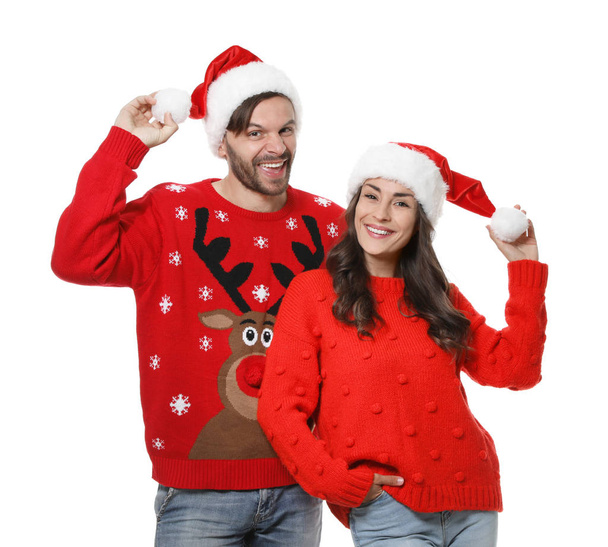 Young couple in Christmas sweaters and hats on white background - Fotó, kép