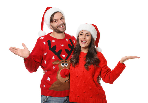 Young couple in Christmas sweaters and hats on white background - Foto, imagen