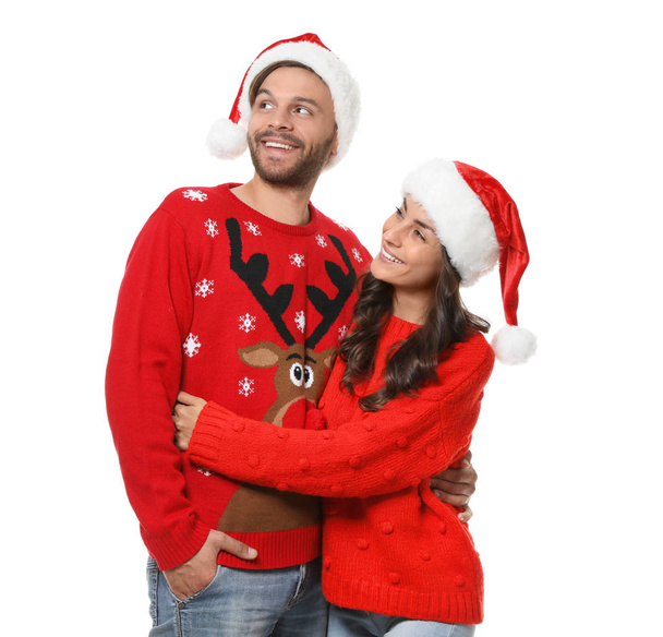 Young couple in Christmas sweaters and hats on white background - Foto, imagen