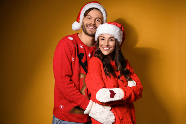 Young couple in Christmas sweaters and hats on yellow background - Фото, зображення