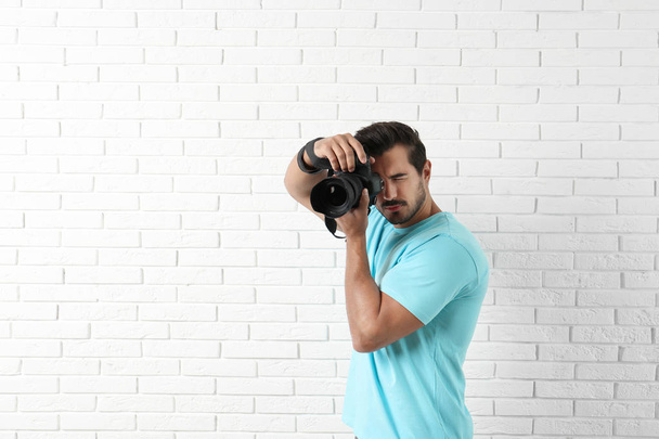 Young professional photographer taking picture near brick wall. Space for text - Foto, Imagen
