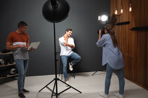 Professional photographer with assistant taking picture of young man in modern studio - Foto, Imagem