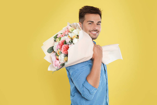 Young handsome man with beautiful flower bouquet on yellow background - Foto, Imagen