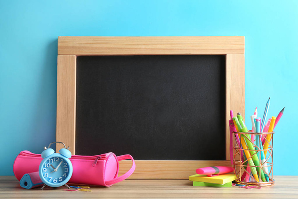 Different school stationery and small blank chalkboard on table near light blue wall. Space for text - Foto, Bild