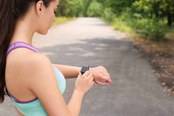 Young woman checking pulse with smartwatch after training in park. Space for text - Fotó, kép