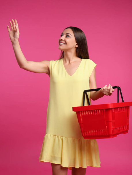 Young woman with empty shopping basket on pink background - Photo, Image