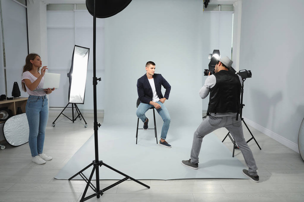Professional photographer with assistant taking picture of young man in modern studio - Φωτογραφία, εικόνα