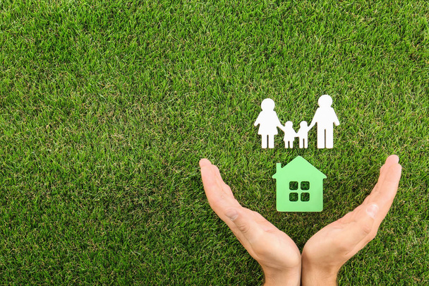 Man Holding handen in de buurt van figuren van huis en familie op groen gras, Top uitzicht. Ruimte voor tekst - Foto, afbeelding