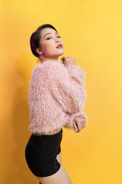 Short-haired girl in fashionable dancing. Young playful female model in stylish fur outfit. Beautiful happy woman having fun dance in studio on yellow - Photo, Image