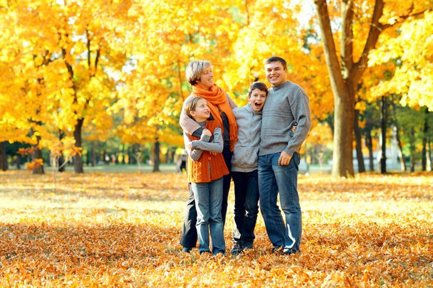 Onnellinen perhe poseeraa, pelaa ja pitää hauskaa syksyllä kaupungin puistossa. Lapset ja vanhemmat viettävät mukavaa päivää yhdessä. Kirkas auringonvalo ja keltaiset lehdet puissa, syyskausi
. - Valokuva, kuva