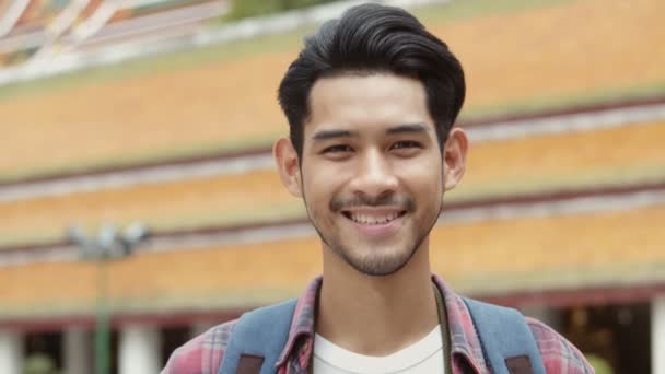 Lächelndes Porträt eines hübschen jungen asiatischen Mannes, der im Tempel Thailand unterwegs ist und ein Foto macht. Asiatische Mann Blogger glücklich genießen Freizeit Lifestylereisen. - Filmmaterial, Video