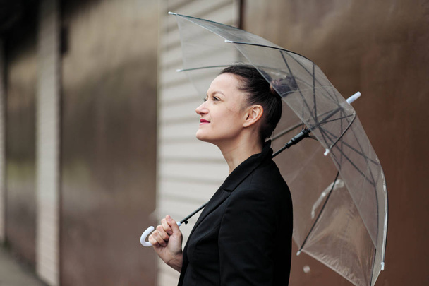 Mladá atraktivní žena v černém kabátku a modrých džínách, které se nacházejí venku na pozadí budovy. - Fotografie, Obrázek
