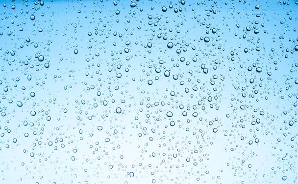 Water druppels op glas op blauwe hemel achtergrond  - Foto, afbeelding