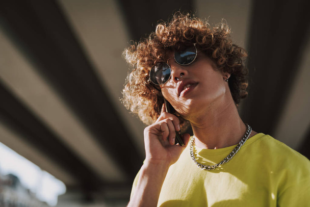 Calm curly young man in sunglasses talking on the phone - Foto, imagen