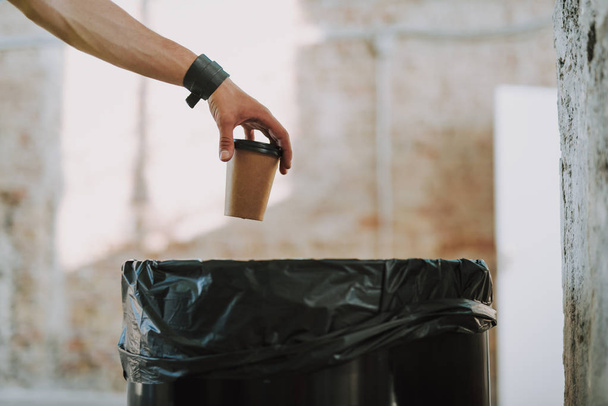 Hand with carton cup of coffee above the rubbish bin - Foto, imagen