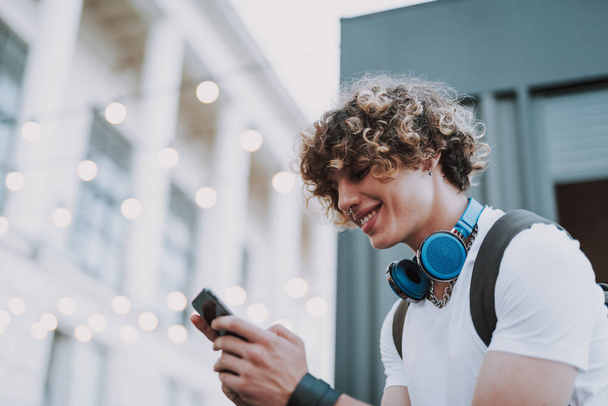 Positive young man is using smartphone outdoors - Fotó, kép