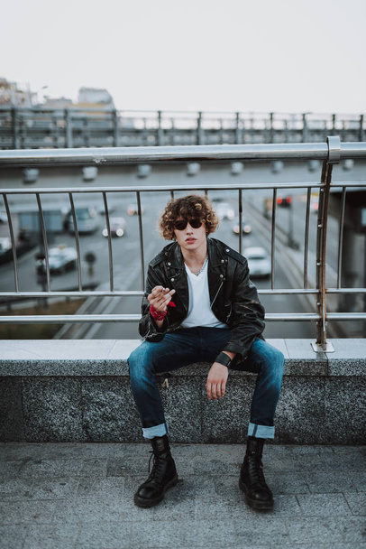 Calm young man sitting on the bridge with cigarette - Valokuva, kuva