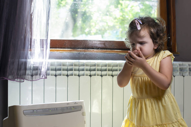 Little girl in a dusty room. Air purifier and coughing kid. Dust - Foto, Imagem