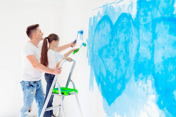 Father and his little daughter painting a wall in new home. - Фото, зображення