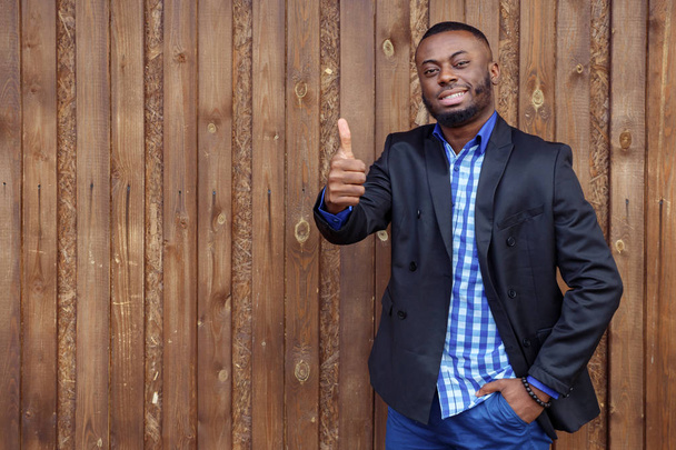 Zwarte Afro Amerikaanse lachende man toont gebaar duim omhoog op donkere houten achtergrond. - Foto, afbeelding