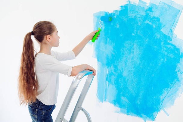Repair in the apartment. Happy child girl paints the wall with blue paint, - Foto, Bild