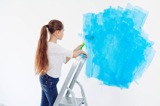 Ремонт в квартире. Счастливая девочка рисует стену синей краской, - Фото, изображение