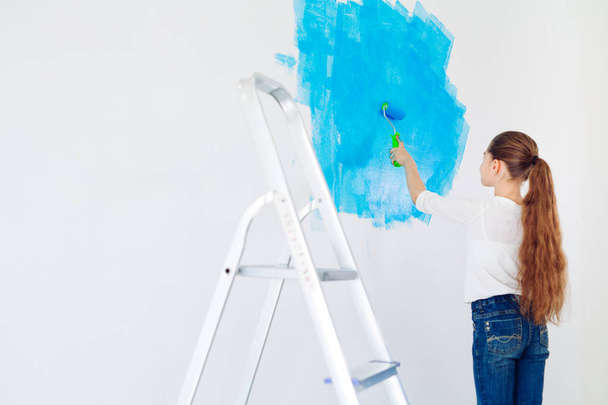 Repair in the apartment. Happy child girl paints the wall with blue paint, - Foto, Bild