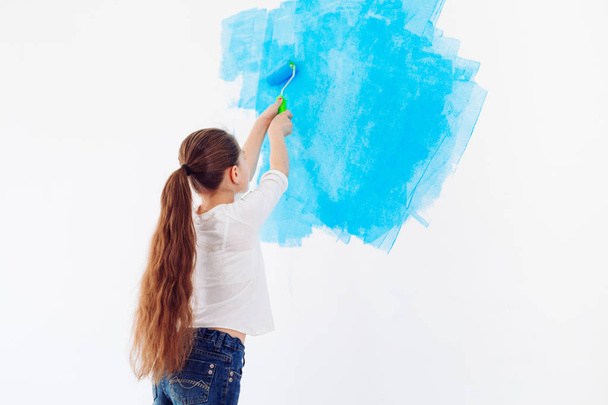 Korjaus asunnossa. Happy lapsi tyttö maalaa seinän sininen maali, - Valokuva, kuva