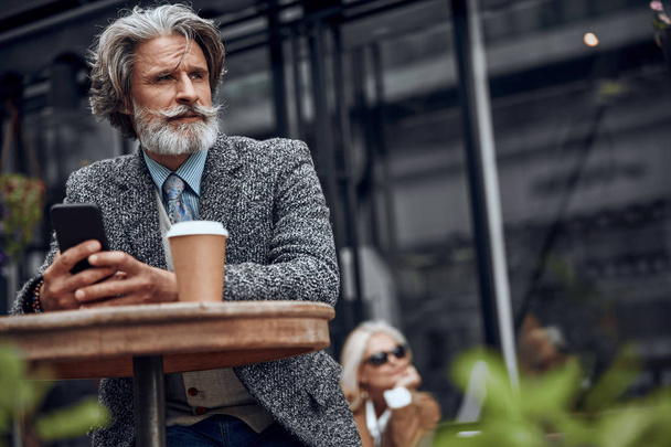 Calm bearded man with smartphone at cafe table stock photo - Valokuva, kuva