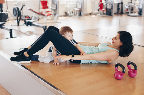 Portret szczęśliwego młodego Fit matka robi ćwiczenia na siłowni i zabawy z jej chłopiec dziecka. Koncepcja zdrowego stylu życia. Sport, macierzyństwo i koncepcja aktywna. - Zdjęcie, obraz