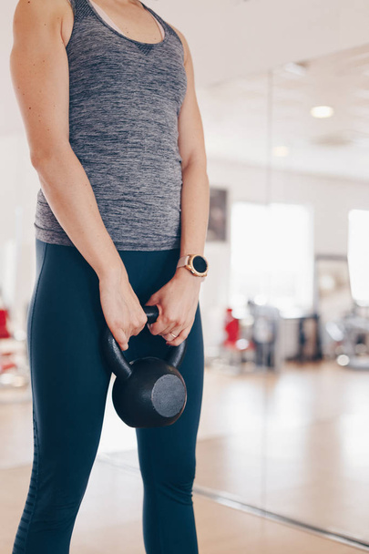 Attractive fit sporty woman working out by lifting kettle bell in the gym, wearing sport watch, Concept of active, sport and healthy living. - Фото, зображення