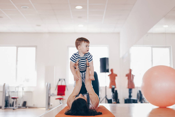 Portrait of happy  young fit mother doing exercise at gym and having fun with her baby boy. Concept of healthy living.  Sport, motherhood and active concept. - Foto, imagen