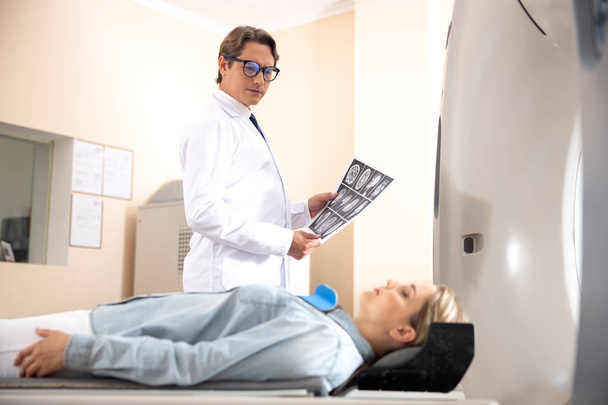 Doctor holding brain CT scan and looking at woman - Foto, imagen
