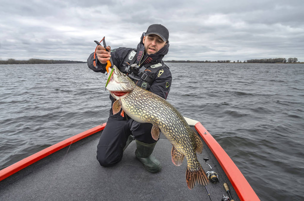 Pike fishing. Happy fisherman with big fish trophy at the boat with tackles - Photo, Image