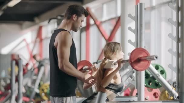 Mujer de fitness en cuclillas en el gimnasio. Entrenador corrector masculino mujer en club deportivo
 - Metraje, vídeo