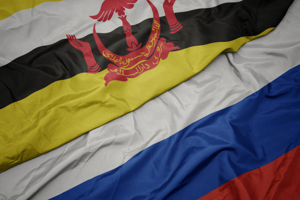 zwaaiende kleurrijke vlag van Rusland en de nationale vlag van Brunei. - Foto, afbeelding