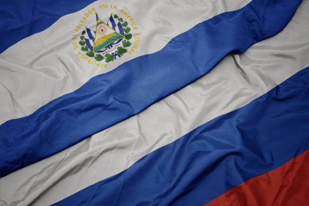 falujące kolorowe flagi Rosji i flagi narodowej Salwadoru. - Zdjęcie, obraz